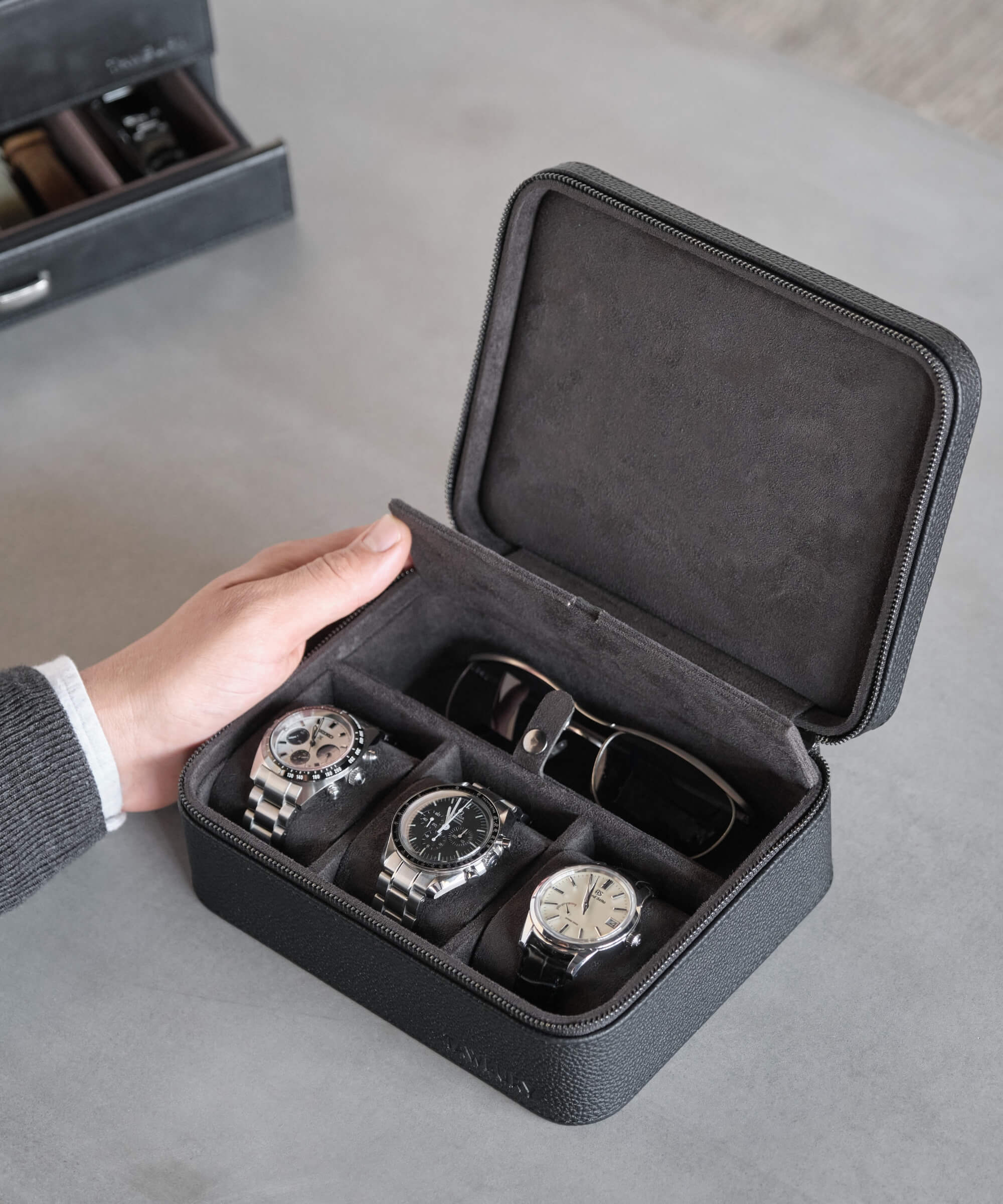 A person with a TAWBURY Fraser 3 Watch Travel Case with Storage - Black, holding a black watch case with four watches inside for convenient storage during their travel experience.