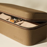 The Fraser 3 Watch Case - Taupe by TAWBURY features textured leather and a partially open zipper displaying a wristwatch inside, making it an ideal stylish storage option for your watches on the go.