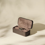 The TAWBURY Fraser 3 Watch Case in brown leather, lined with brown suede, sits open on a beige surface with soft shadows.