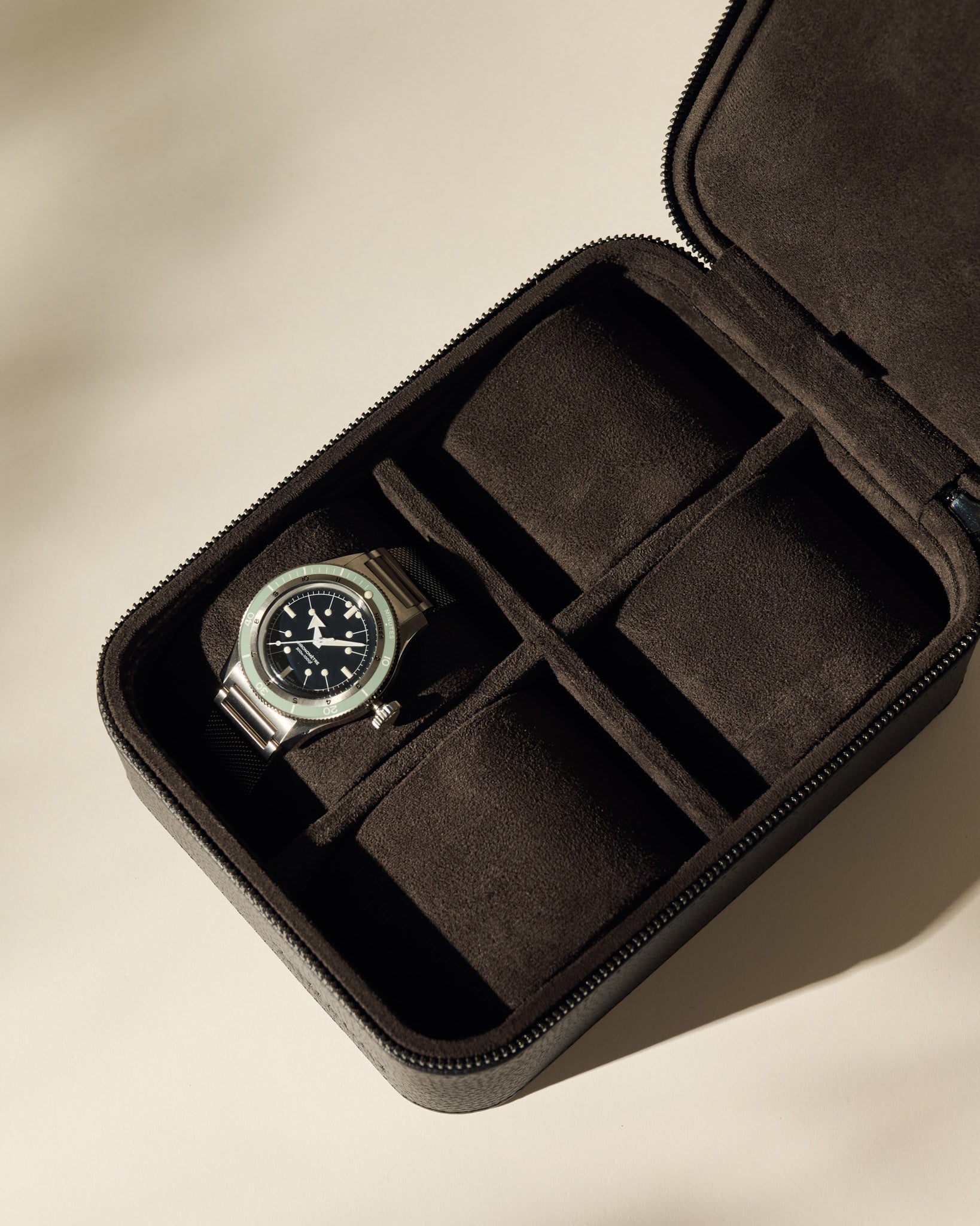 A TAWBURY Fraser 4 Watch Case - Black holds a wristwatch with a metal band, while its other three compartments are empty.