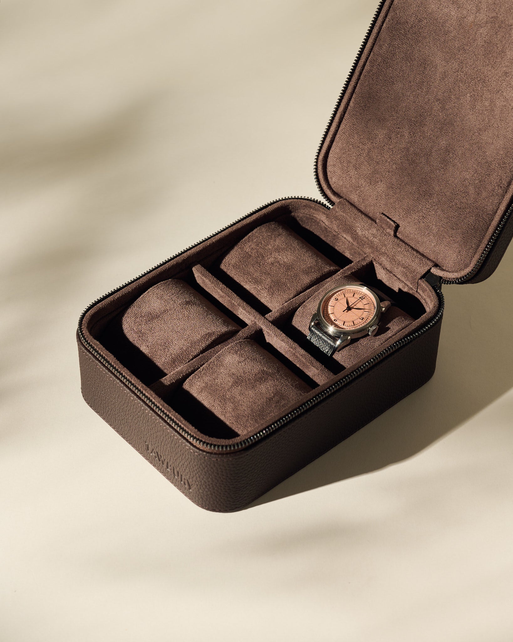 The TAWBURY Fraser 4 Watch Case - Brown features leather construction, a suede interior, and storage for four watches; one wristwatch with a copper face is stored inside, leaving three compartments free—perfect for stylish travel.
