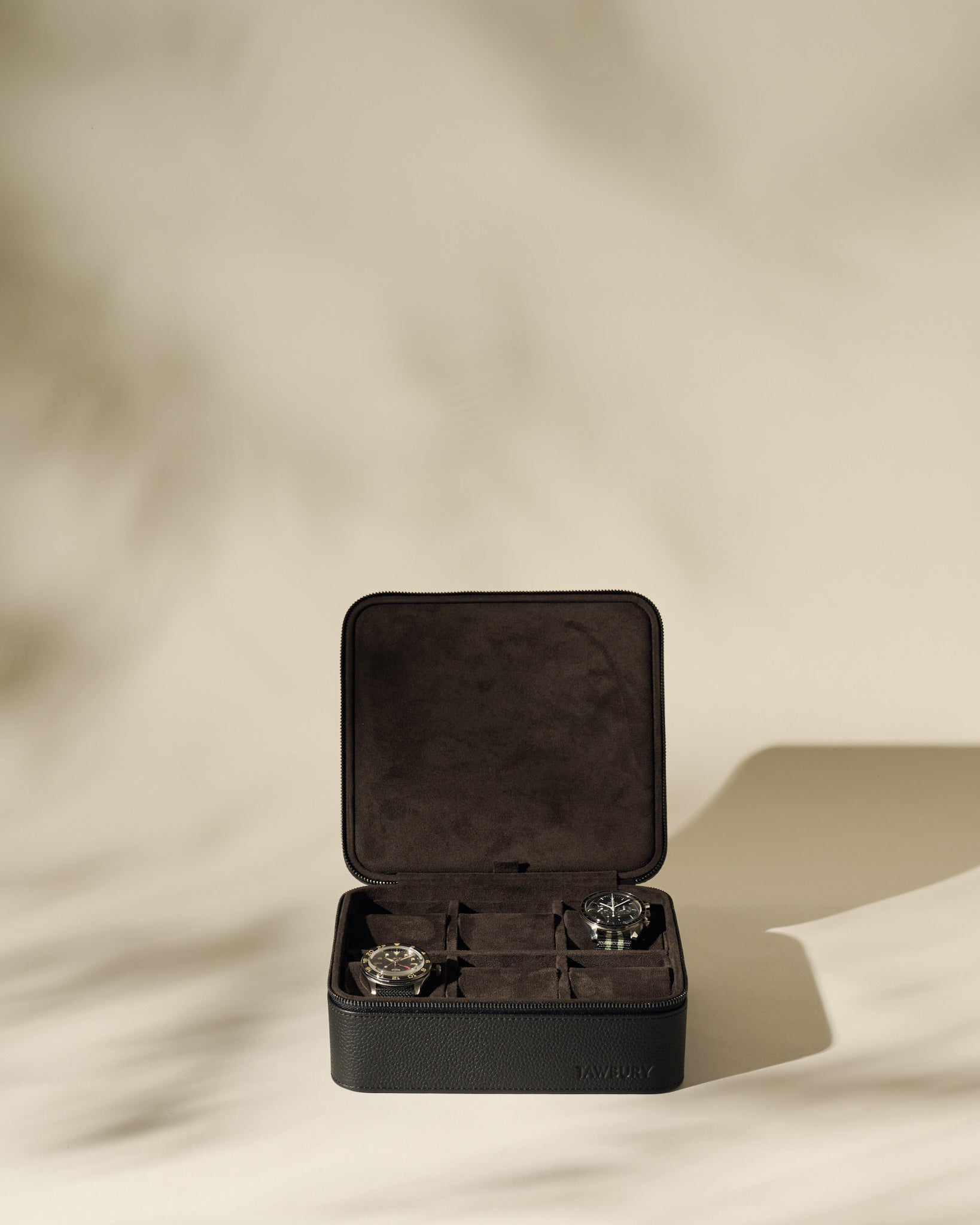 The TAWBURY Fraser 6 Watch Case in black leather with a suede interior is shown open on a neutral background, displaying two wristwatches inside amid soft shadows.