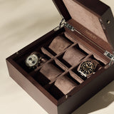 A TAWBURY Grove 6 Slot Wooden Watch Box in dark walnut wood with a solid lid displays two wristwatches. The open box reveals the brand name "TAWBURY" inside its velvet-lined, elegant compartments for more timepieces.