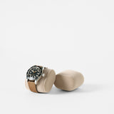 The TAWBURY Bayswater Watch Pillows in beige (55mm, X-Small) are shown: one holds a brown leather strap wristwatch and the other lies empty, both inspired by slender wrist watch pillows, set against a white background.