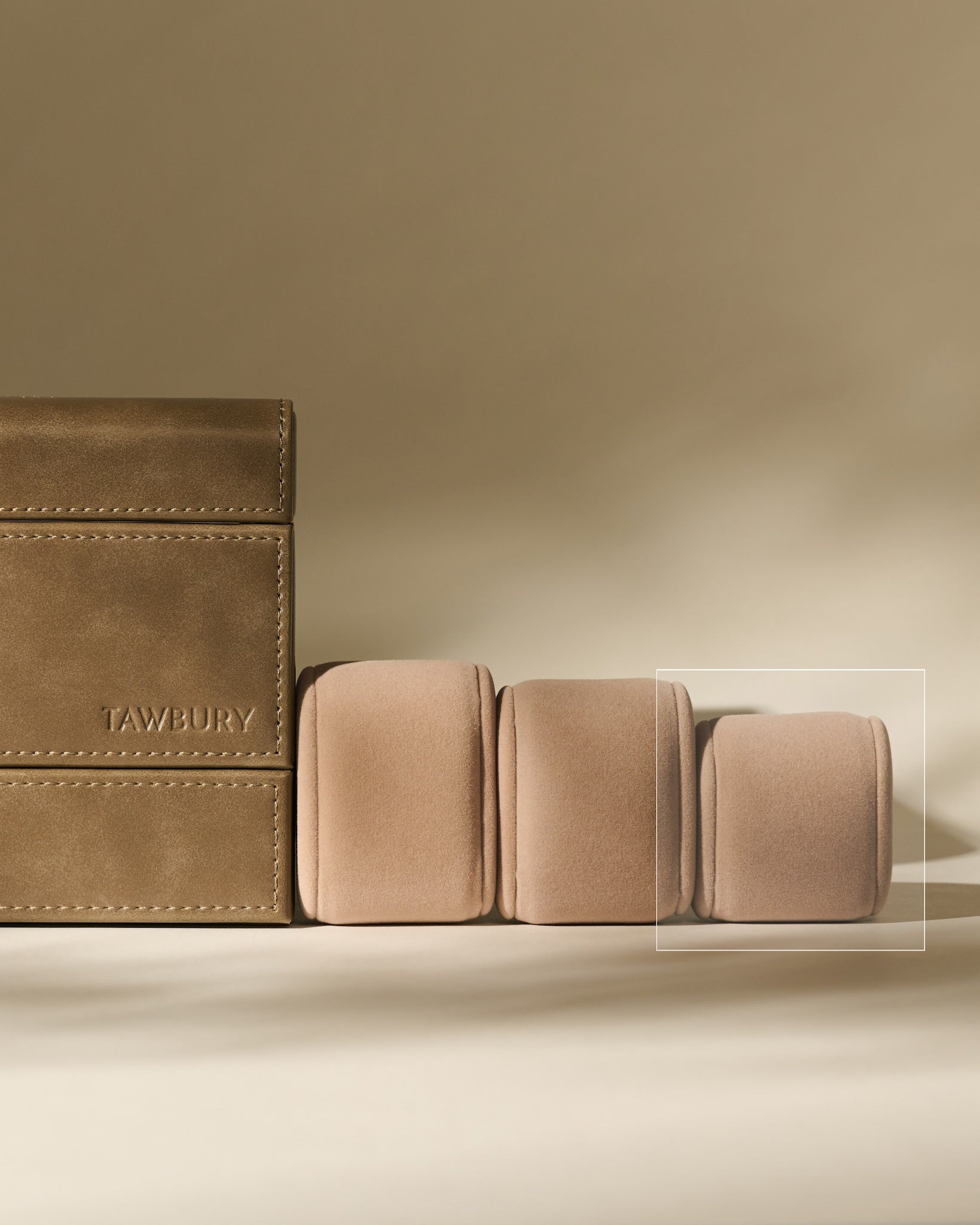 A TAWBURY brown leather box sits beside three Bayswater Watch Pillows in beige (50mm, X-Small), arranged on a neutral background.