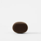 A TAWBURY Bayswater Watch Pillow in Graphite (55mm, X-Small), oval-shaped and foam, is centered on a white background with a soft shadow beneath it.
