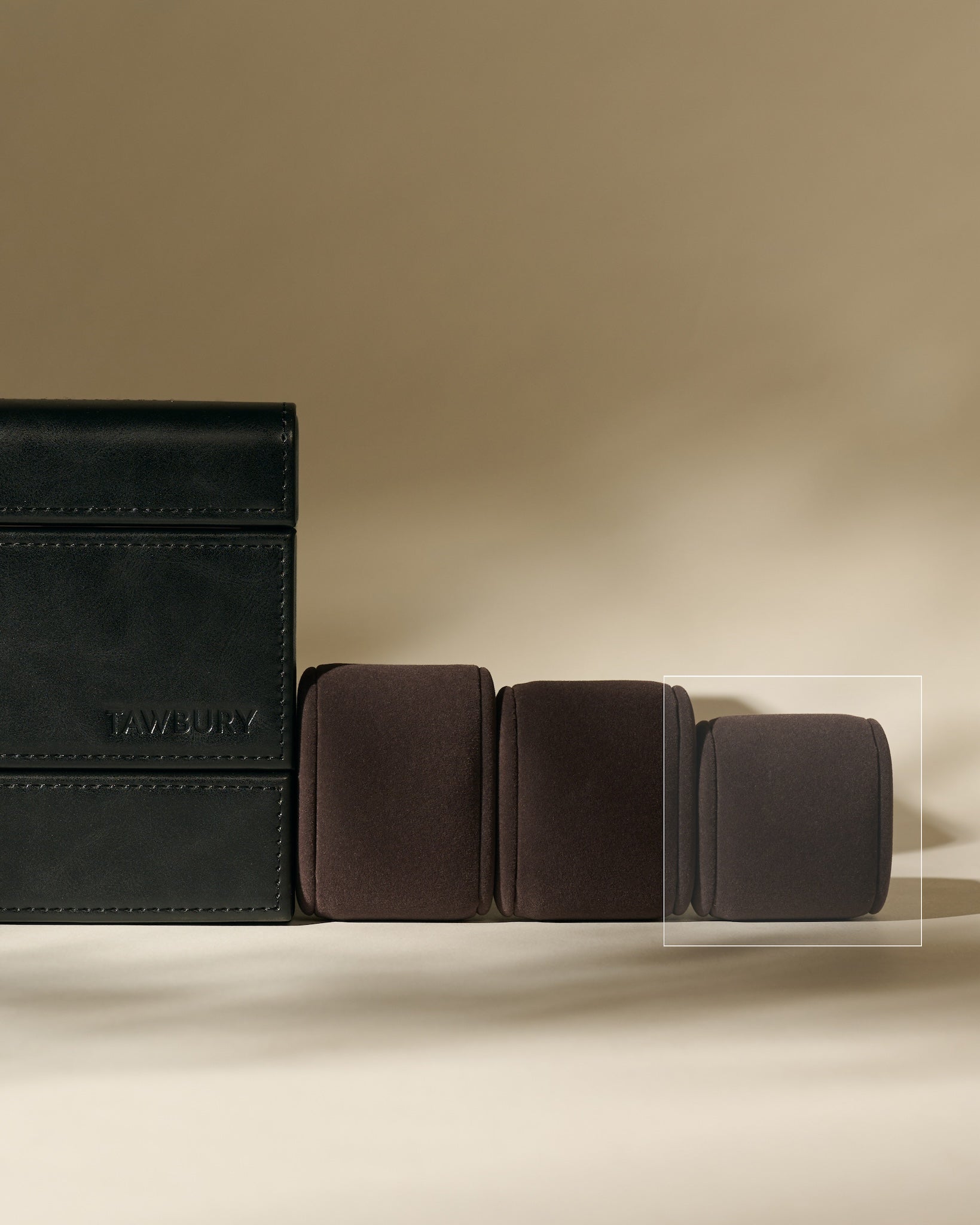 Three TAWBURY Bayswater Watch Pillows in Charcoal (55mm, X-Small) sit beside a black leather watch box, all arranged on a neutral background.