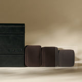 Three charcoal Bayswater Watch Pillows (50mm, X-Small) by TAWBURY sit beside a black leather watch case embossed with "TAWBURY" on a beige surface, ideal as elegant accessories for your watch box.