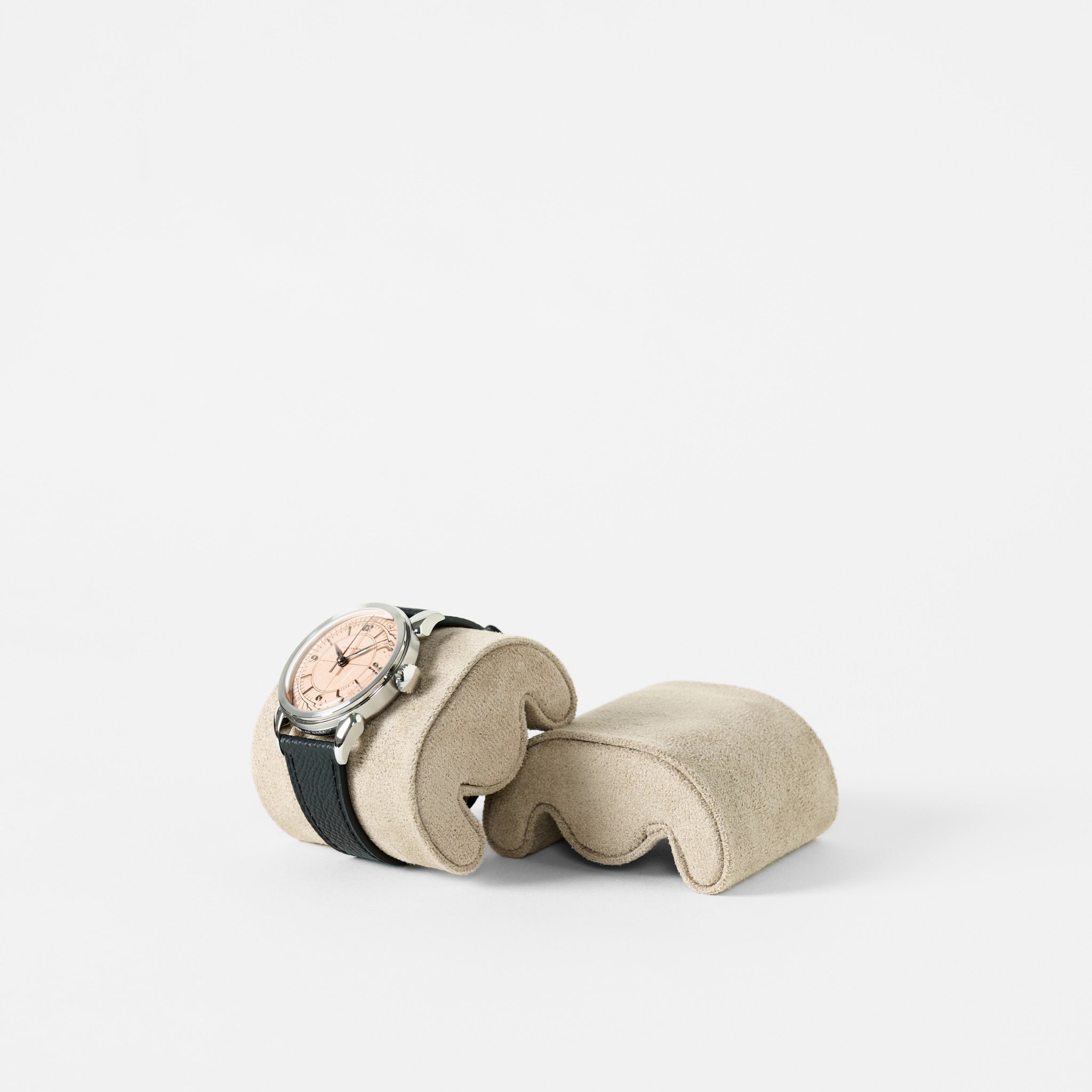 A wristwatch with a light face and black strap rests on a TAWBURY Fraser Watch Pillow (X-Small, Beige), displayed against a plain white background.