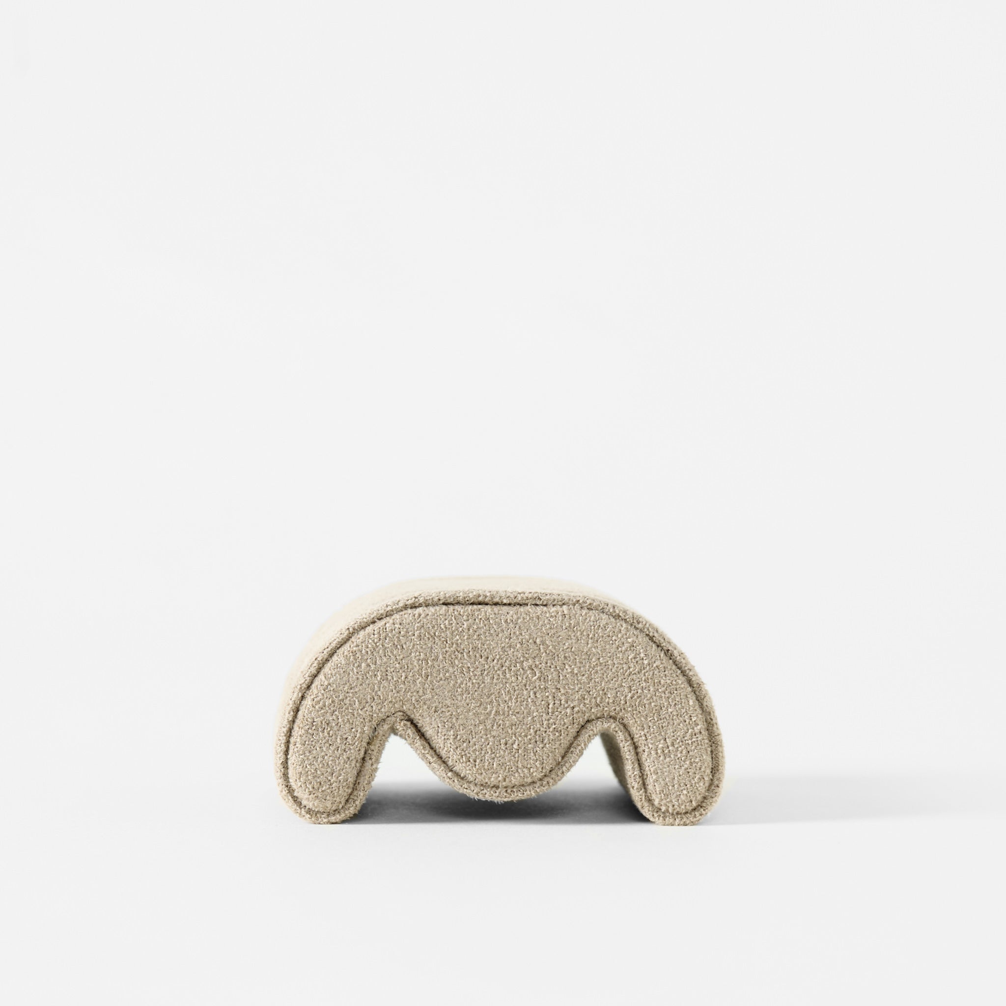 A small, beige, curved TAWBURY Fraser Watch Pillow (X-Small) with a textured surface is displayed against a white background.