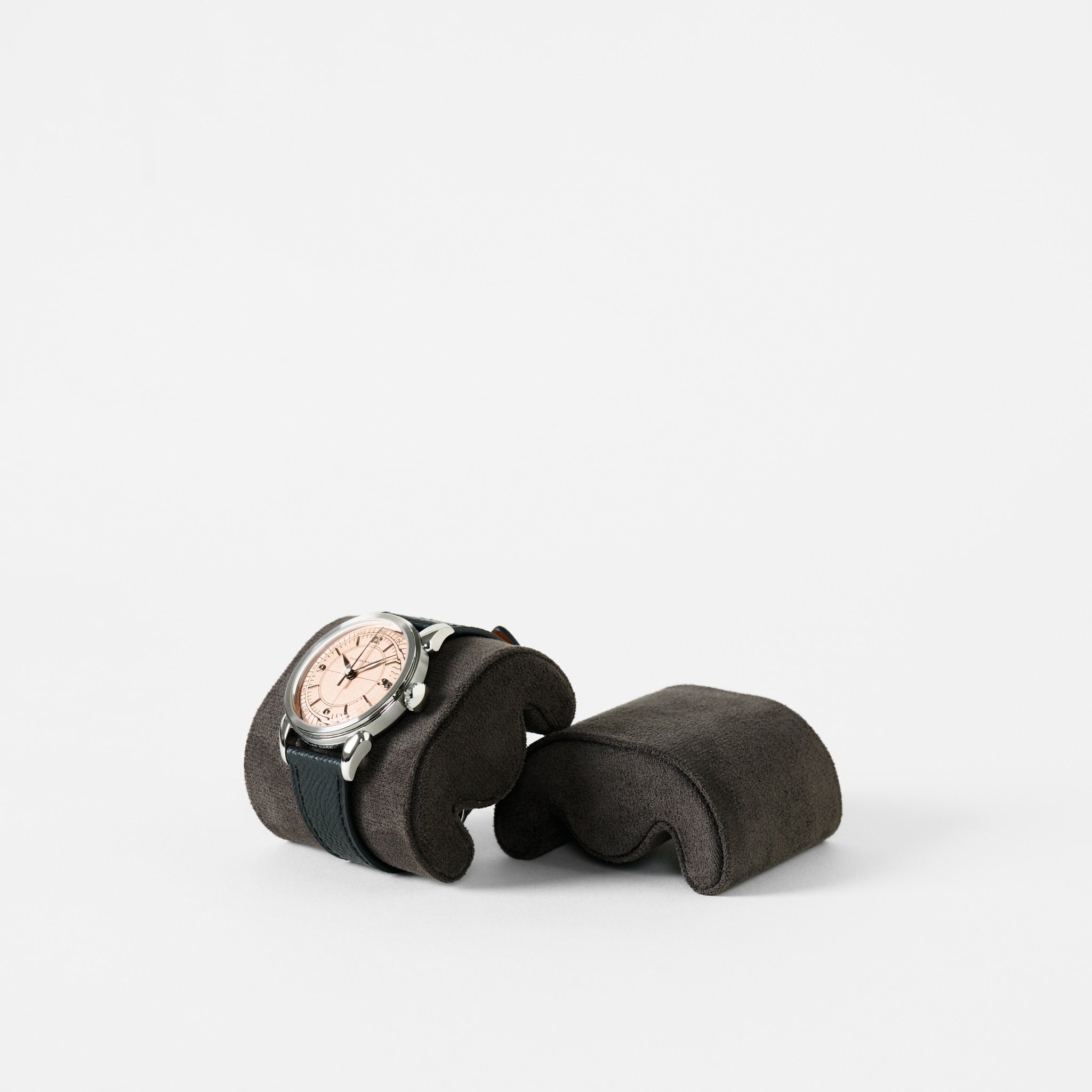 A wristwatch with a black strap and light dial rests on a TAWBURY Fraser Watch Pillow (X-Small, Anthracite), displayed against a plain white background.