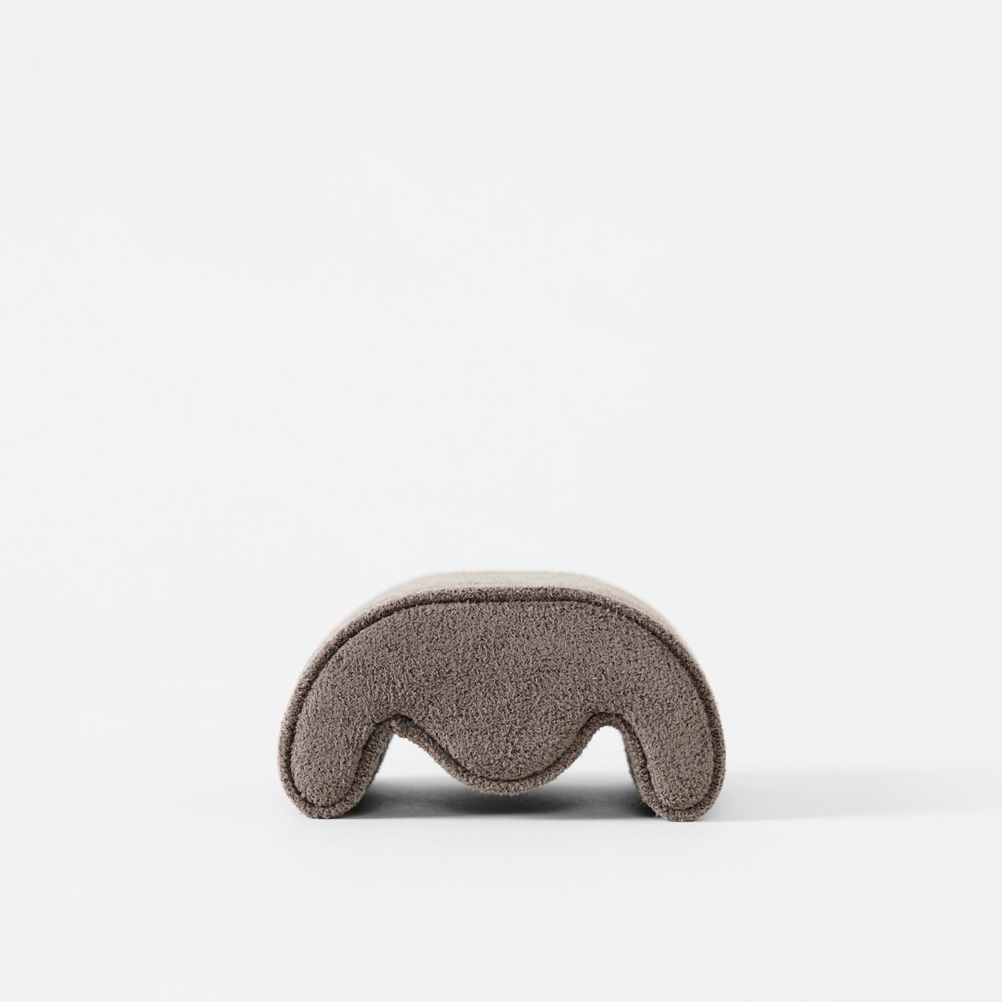 A small, brown, curved object with a suede-like texture—identified as a Fraser Watch Pillow (X-Small, Brown) by TAWBURY—is displayed on a plain white background.