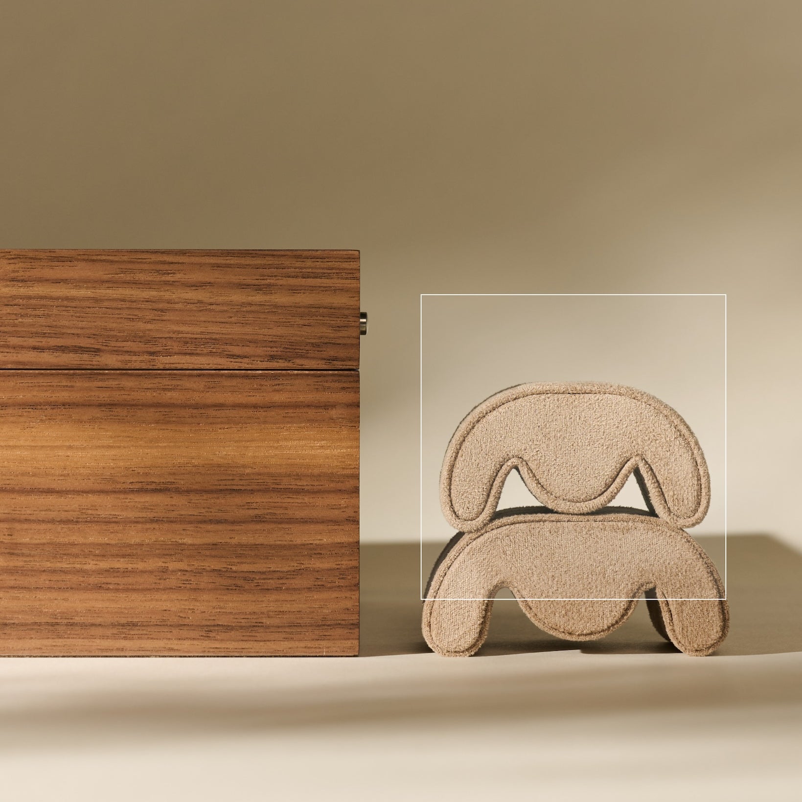 A TAWBURY Grove Watch Pillow in X-Small Beige sits beside a metallic wire sculpture shaped like a stylized dog, both casting shadows on a beige background.