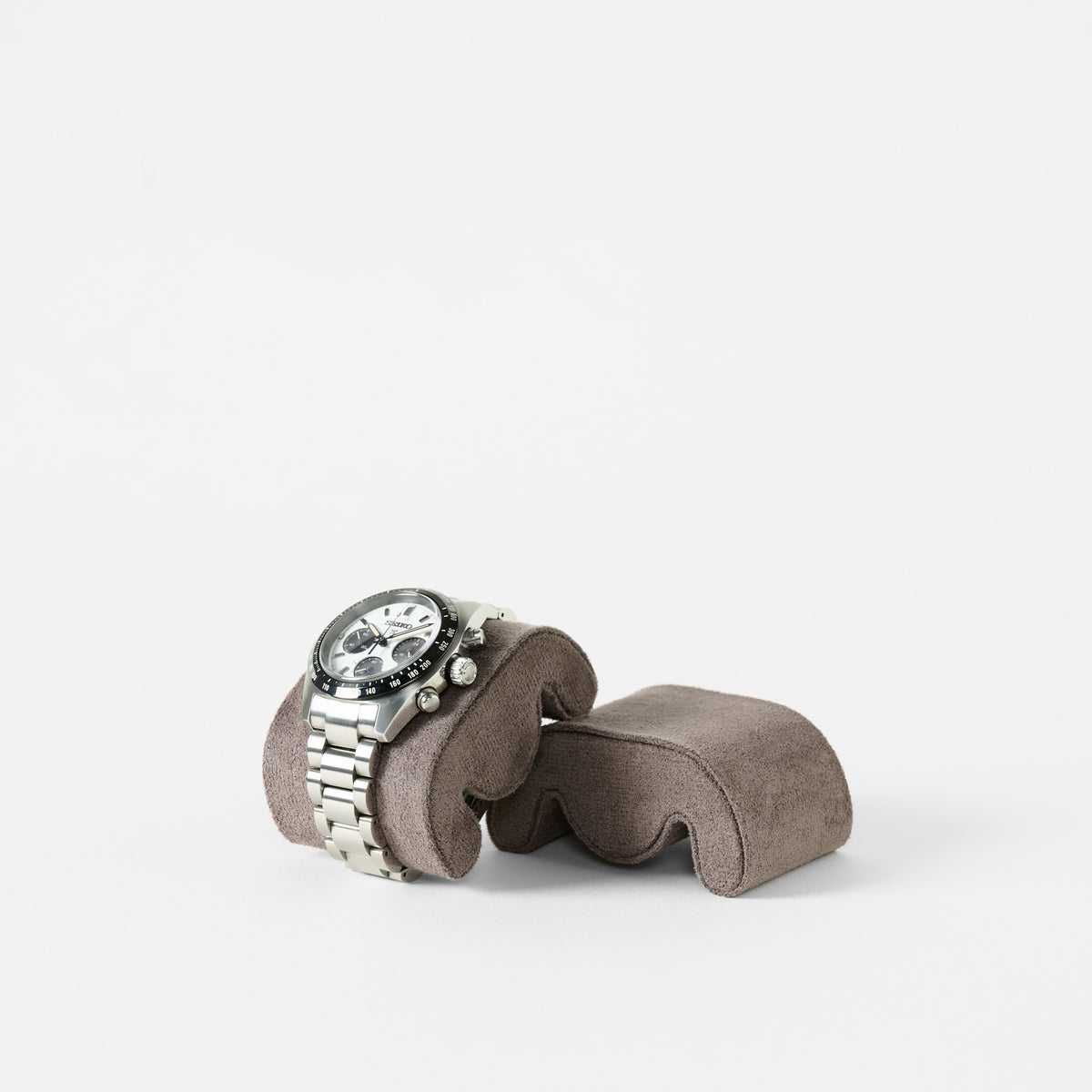A silver wristwatch with a white face and three subdials is displayed on a TAWBURY Grove Watch Pillow - Standard - Brown against a plain white background.