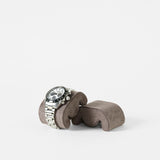 A silver wristwatch with a white face and three subdials is displayed on a TAWBURY Grove Watch Pillow - Standard - Brown against a plain white background.