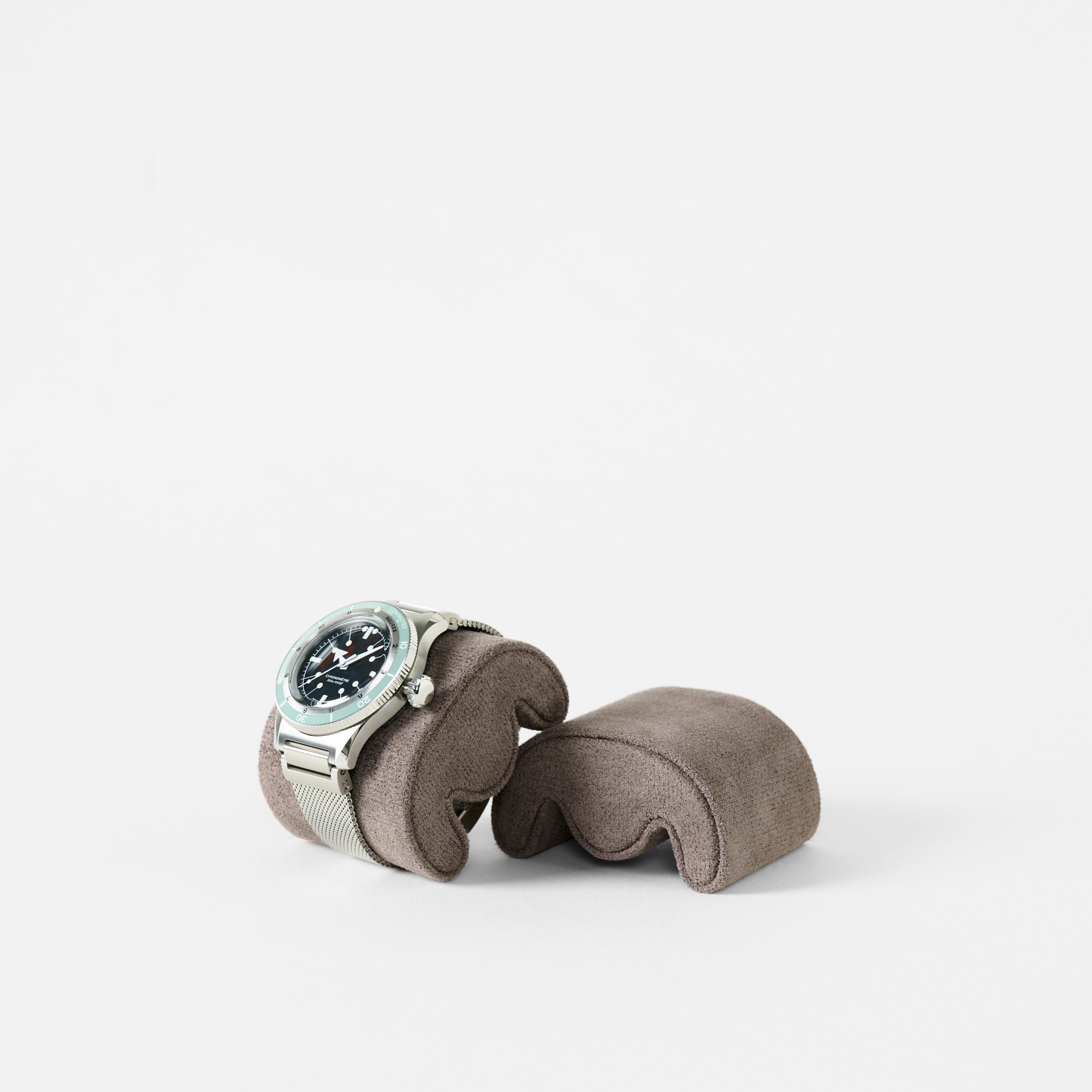 The TAWBURY Grove Watch Pillows - X-Small in brown displays a silver wristwatch with a black face, ideal for slender wrists, against a plain white background.