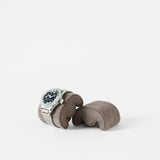 The TAWBURY Grove Watch Pillows - X-Small in brown displays a silver wristwatch with a black face, ideal for slender wrists, against a plain white background.