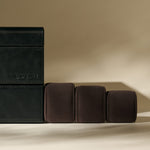 The TAWBURY Bayswater 6 Watch Jewelry Box in midnight black is displayed beside three brown velvet watch pillows on a beige background.