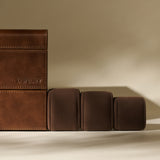 The TAWBURY Bayswater 24 Slot Watch Box with Drawer in Chestnut Brown is shown alongside three brown cushioned watch pillows on a neutral background, highlighting elegant watch storage.