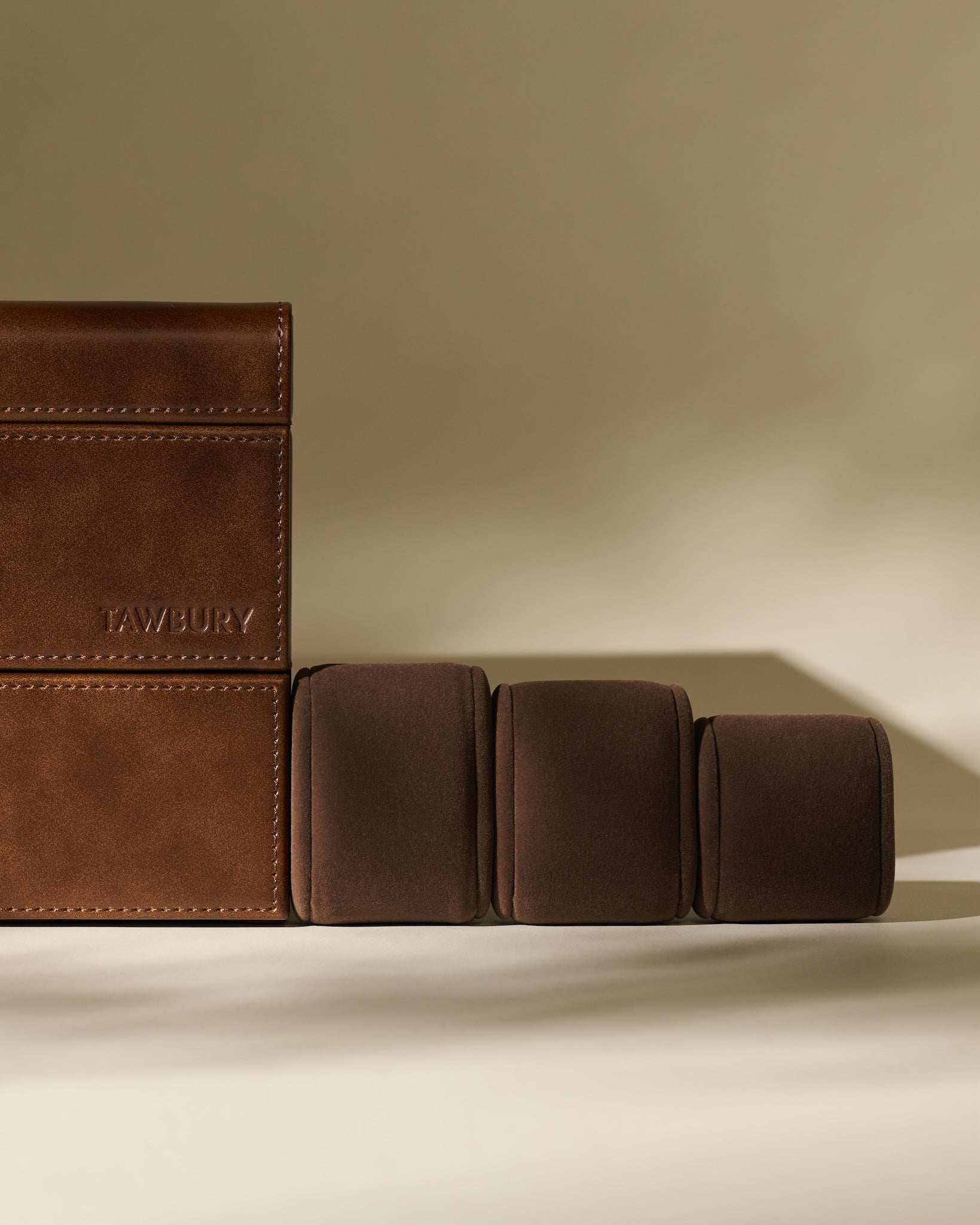 The TAWBURY Bayswater 24 Slot Watch Box with Drawer in Chestnut Brown is shown alongside three brown cushioned watch pillows on a neutral background, highlighting elegant watch storage.