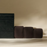 The TAWBURY Bayswater 8 Slot Watch Box with Storage in Midnight Black is shown beside three brown cushioned watch rolls on a beige background—perfect for elegant watch organization.
