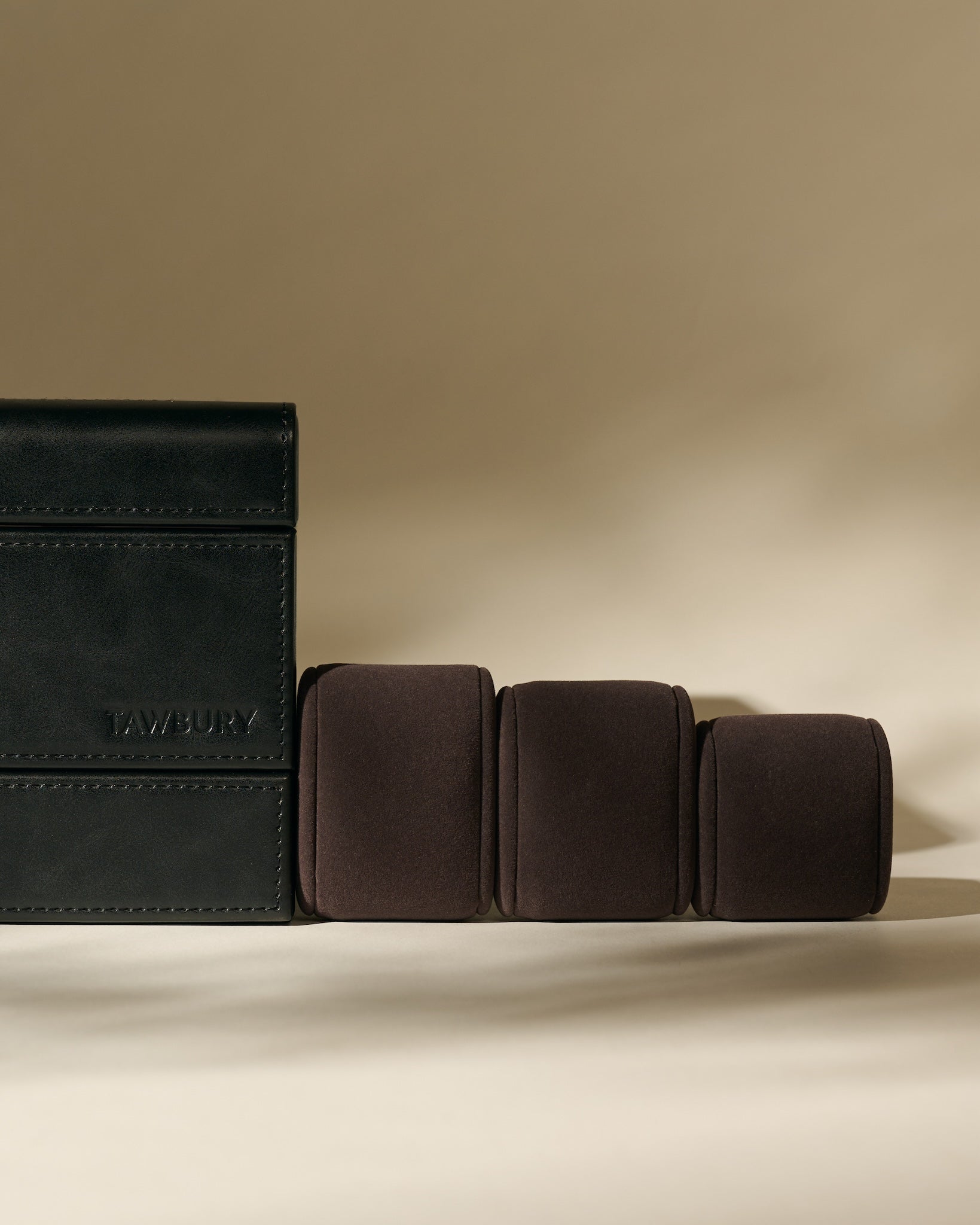 The TAWBURY Bayswater 8 Slot Watch Box with Storage in Midnight Black is shown beside three brown cushioned watch rolls on a beige background—perfect for elegant watch organization.