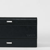 The Bayswater 8 Slot Watch Box with Storage by TAWBURY features a rectangular black/charcoal design, subtle stitching, two silver handles, and the TAWBURY logo embossed on the lower right—ideal for stylish watch storage.