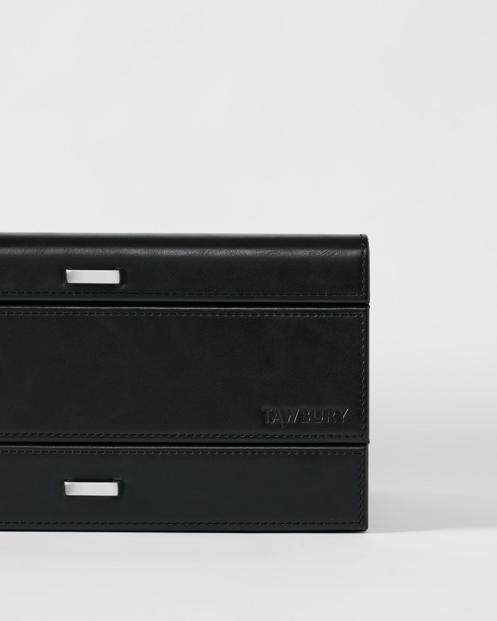 The Bayswater 8 Slot Watch Box with Storage by TAWBURY features a rectangular black/charcoal design, subtle stitching, two silver handles, and the TAWBURY logo embossed on the lower right—ideal for stylish watch storage.