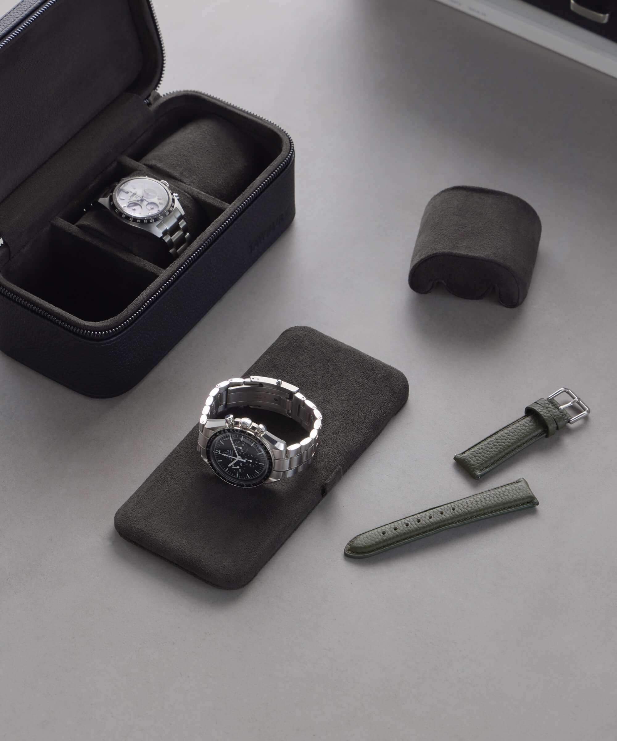 The Fraser 3 Watch Travel Case by TAWBURY elegantly showcases two watches on black pillows, one protected in a leather case, alongside a green strap, extra clasp, and box lid—all arranged on a gray surface—perfect for your next adventure.