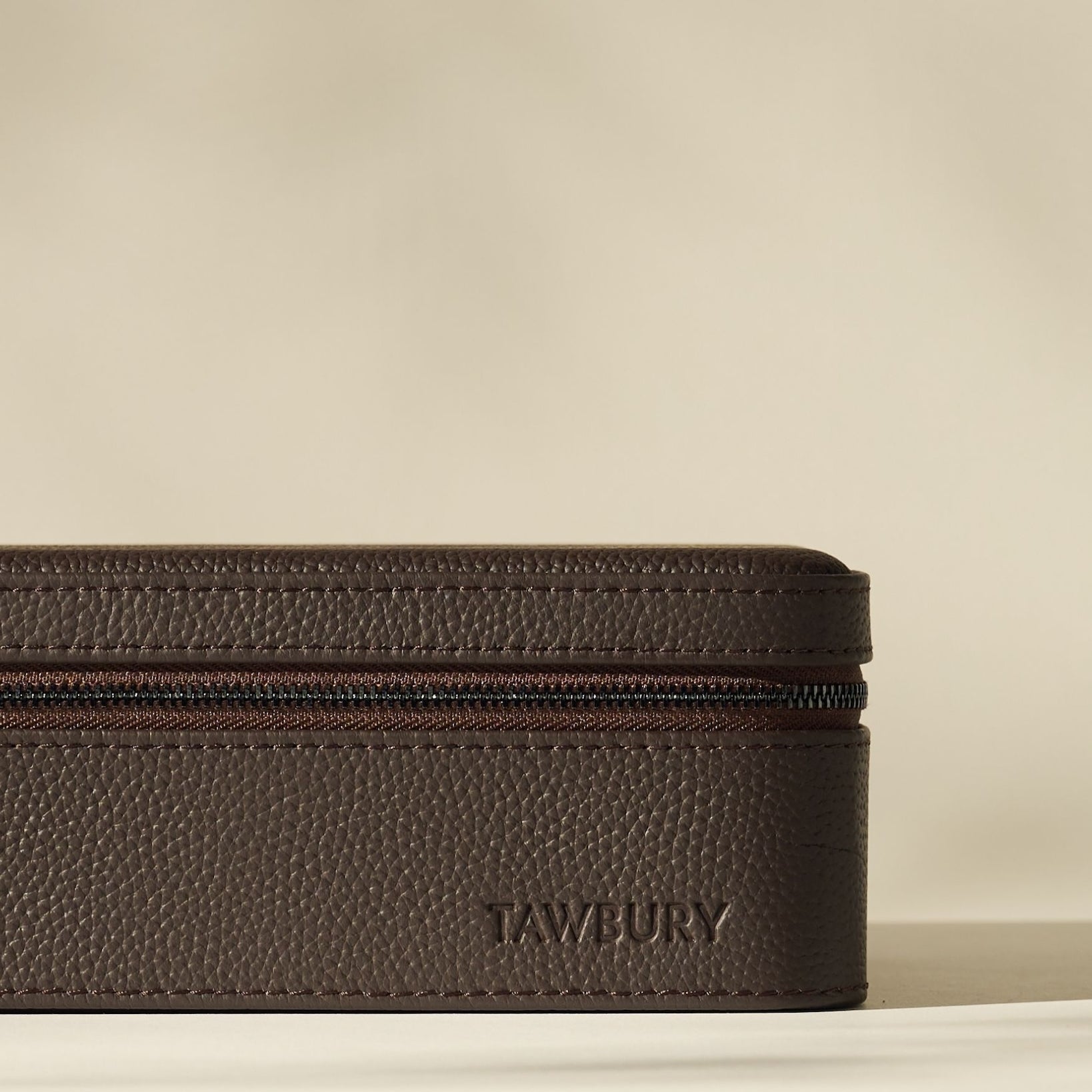 The Fraser 8 Watch Case by TAWBURY features a brown textured rectangular leather design with the brand embossed on the side, displayed against a plain beige background.