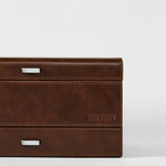 Close-up of the TAWBURY Bayswater 8 Slot Watch Box with Storage in brown faux leather, featuring metal handles and "TAWBURY" embossed on the lower right corner, set against a plain white background.