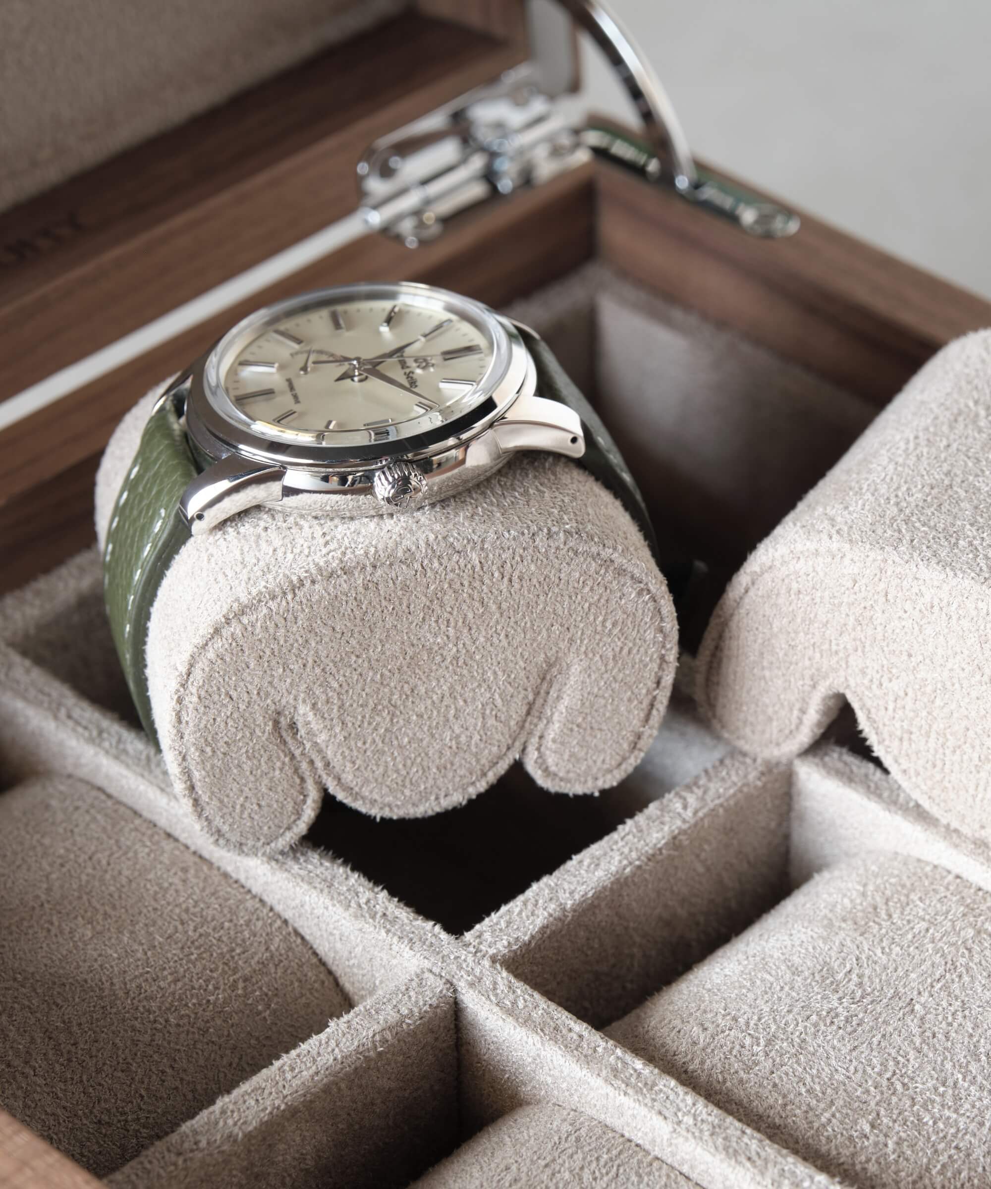 A TAWBURY watch from the Grove 6 Slot Watch Box with Solid Lid - Walnut collection is sitting in a wooden box filled with other timepieces.