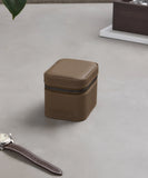The TAWBURY Fraser 1 Watch Travel Case in taupe sits on a light gray surface beside a wristwatch with a matching brown leather strap.