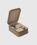 A Fraser 4 Watch Travel Case - Taupe (Coming Soon) from TAWBURY features a tan, textured exterior that opens to reveal two watches inside on soft beige compartments.