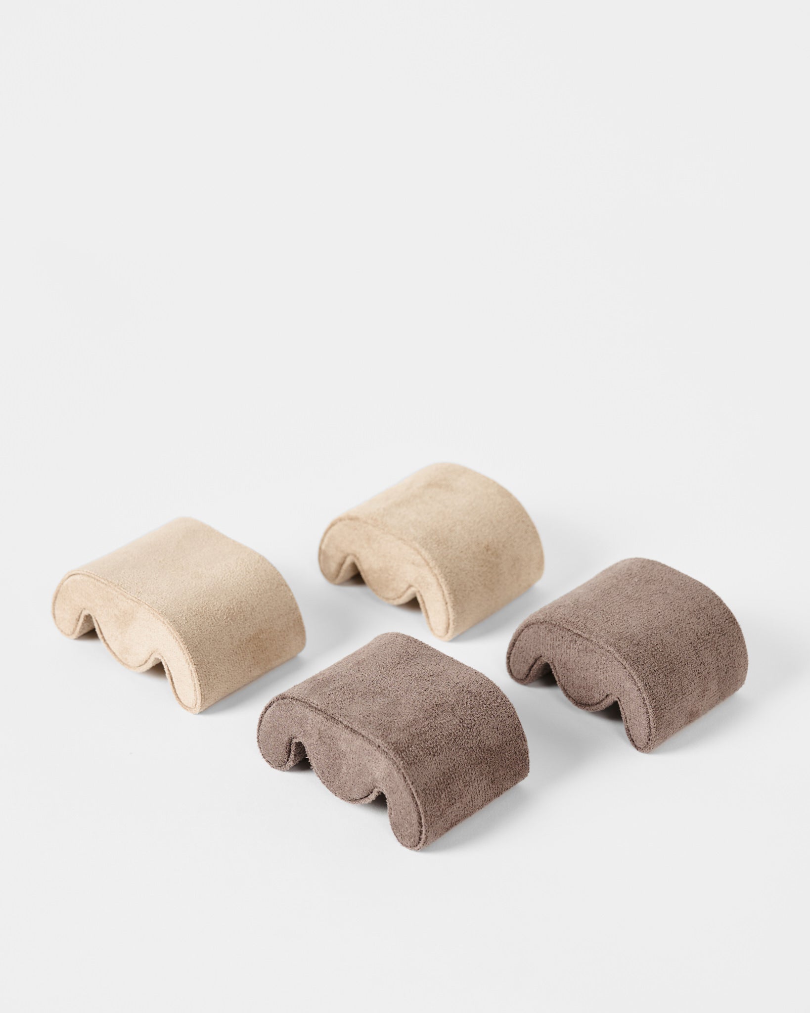 Four curved, rectangular beige and brown foam pads by TAWBURY, ideal for use in the Grove 6 Slot Wooden Watch Box - Light Walnut Wood - Solid Lid or any display case, displayed on a plain white background.