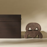 A TAWBURY Grove 6 Slot Wooden Watch Box in Dark Walnut Wood with a Glass Lid stands beside two stacked, curved, brown objects on a neutral background.
