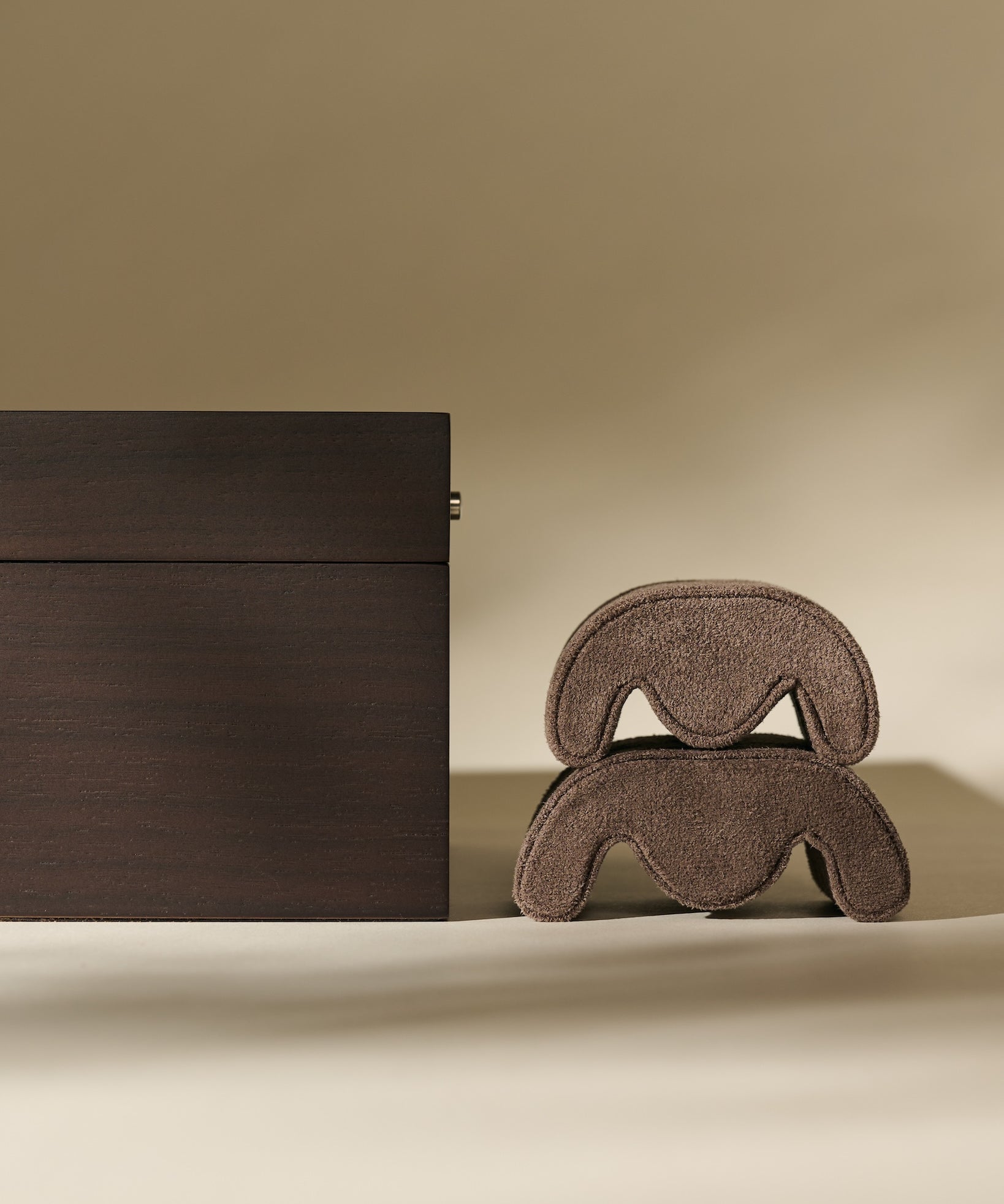 A TAWBURY Grove 6 Slot Wooden Watch Box in Dark Walnut Wood with a Glass Lid stands beside two stacked, curved, brown objects on a neutral background.