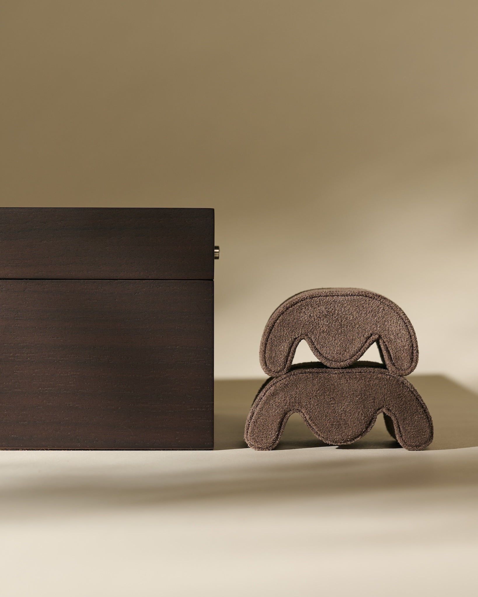 A TAWBURY Grove 6 Slot Wooden Watch Box in Dark Walnut Wood with a Glass Lid stands beside two stacked, curved, brown objects on a neutral background.