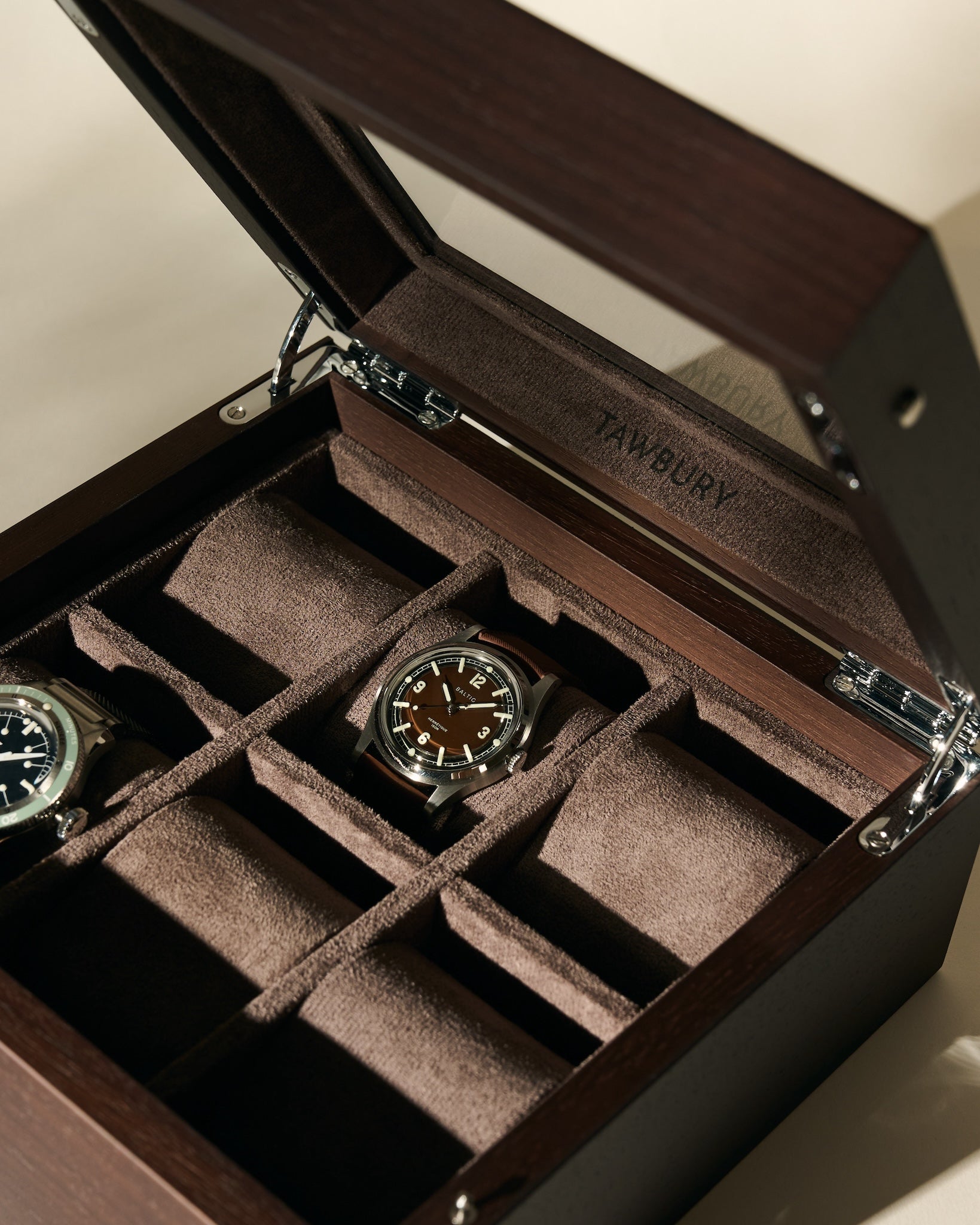 The TAWBURY Grove 6 Slot Wooden Watch Box in dark walnut features a glass lid and multiple suede-lined compartments, stylishly organizing and displaying your timepieces, with two watches shown separately.