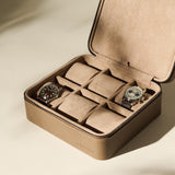 The TAWBURY Fraser 6 Watch Case in taupe leather features a suede interior, offering elegant storage for up to six watches—two compartments currently hold wristwatches, while the others remain empty.