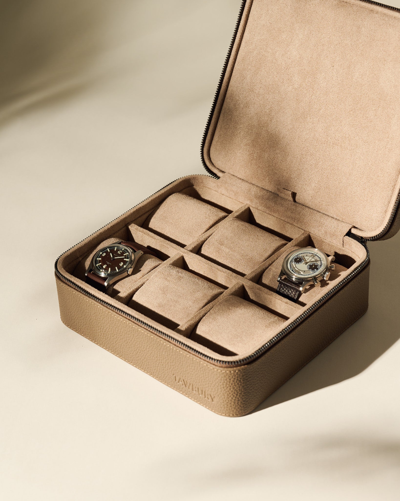 The TAWBURY Fraser 6 Watch Case in taupe leather features a suede interior, offering elegant storage for up to six watches—two compartments currently hold wristwatches, while the others remain empty.
