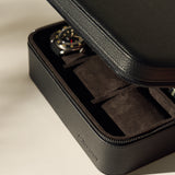 The TAWBURY Fraser 6 Watch Case in black features a partially open zipper, revealing a wristwatch inside on a soft, dark interior—ideal for elegant watch storage.