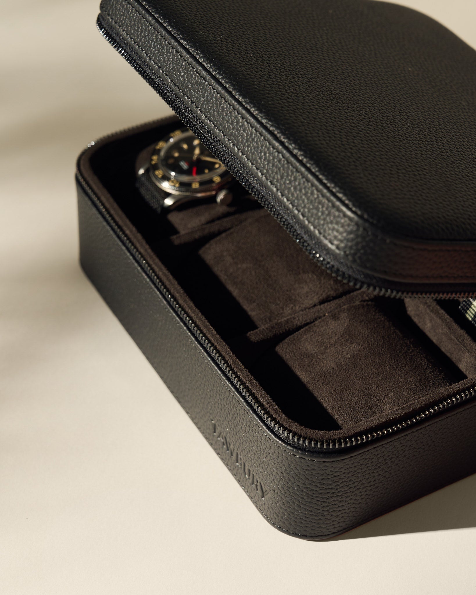 The TAWBURY Fraser 6 Watch Case in black features a partially open zipper, revealing a wristwatch inside on a soft, dark interior—ideal for elegant watch storage.