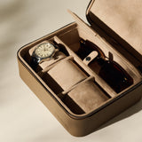 The TAWBURY Fraser 3 Watch Case with Storage in taupe features a beige suede interior, neatly organizing a wristwatch and sunglasses in separate compartments—perfect for stylish travel.