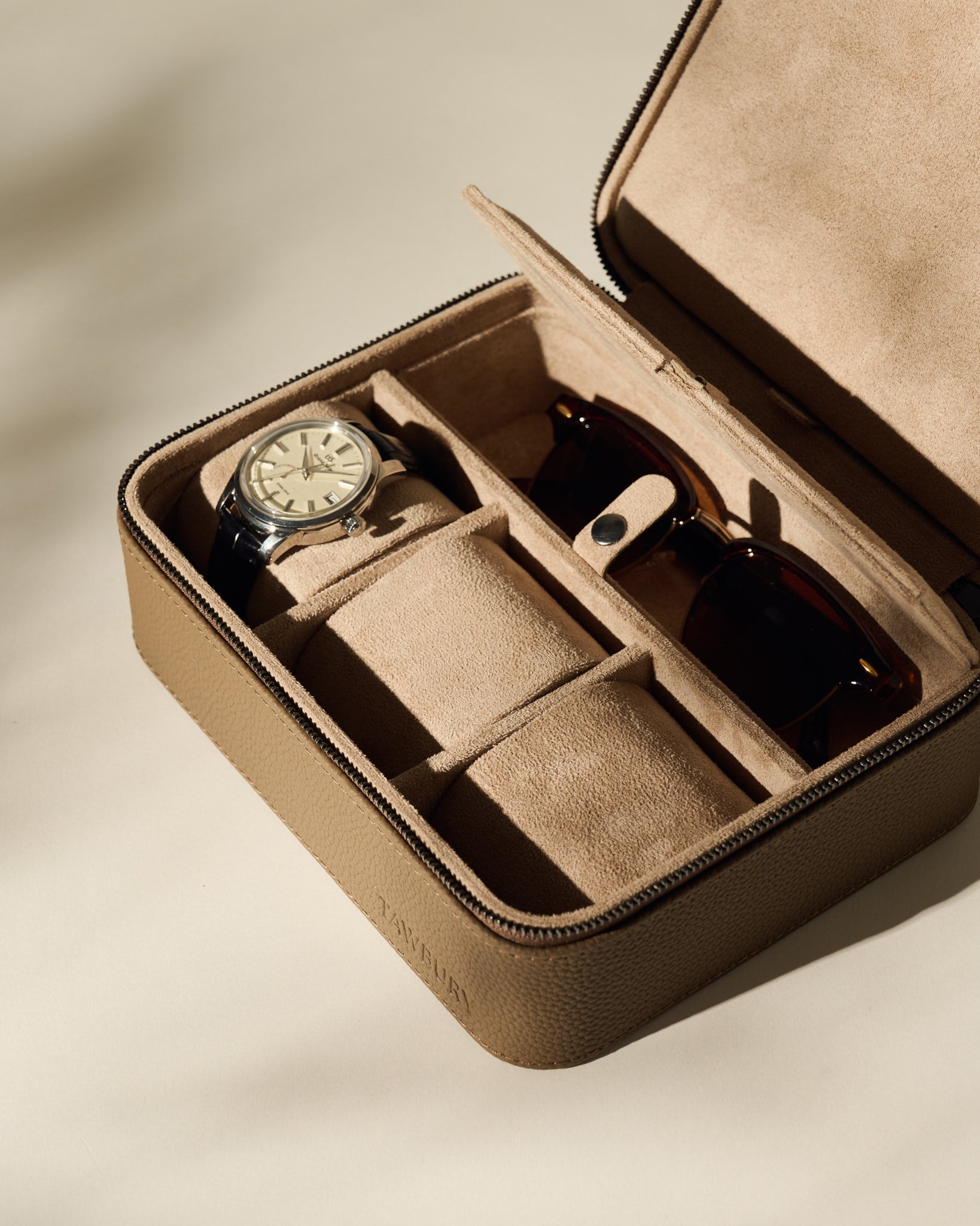 The TAWBURY Fraser 3 Watch Case with Storage in taupe features a beige suede interior, neatly organizing a wristwatch and sunglasses in separate compartments—perfect for stylish travel.