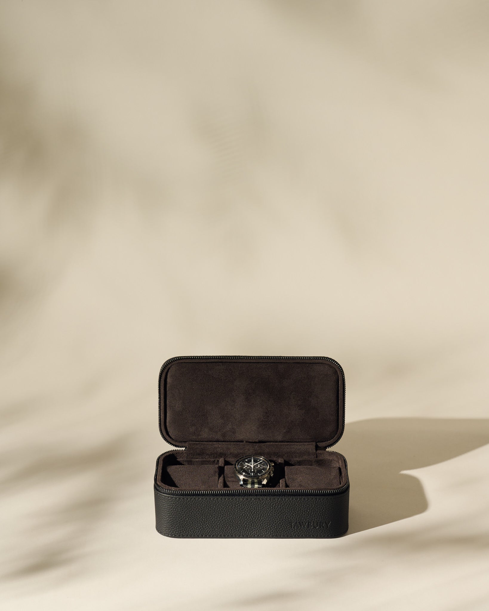 The TAWBURY Fraser 3 Watch Case - Black, with a soft interior, is shown on a beige background with gentle shadows—ideal for storing your watches during travel.
