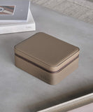 A TAWBURY Fraser 3 Watch Travel Case with Storage - Taupe, offering protection, placed on a table next to a book.