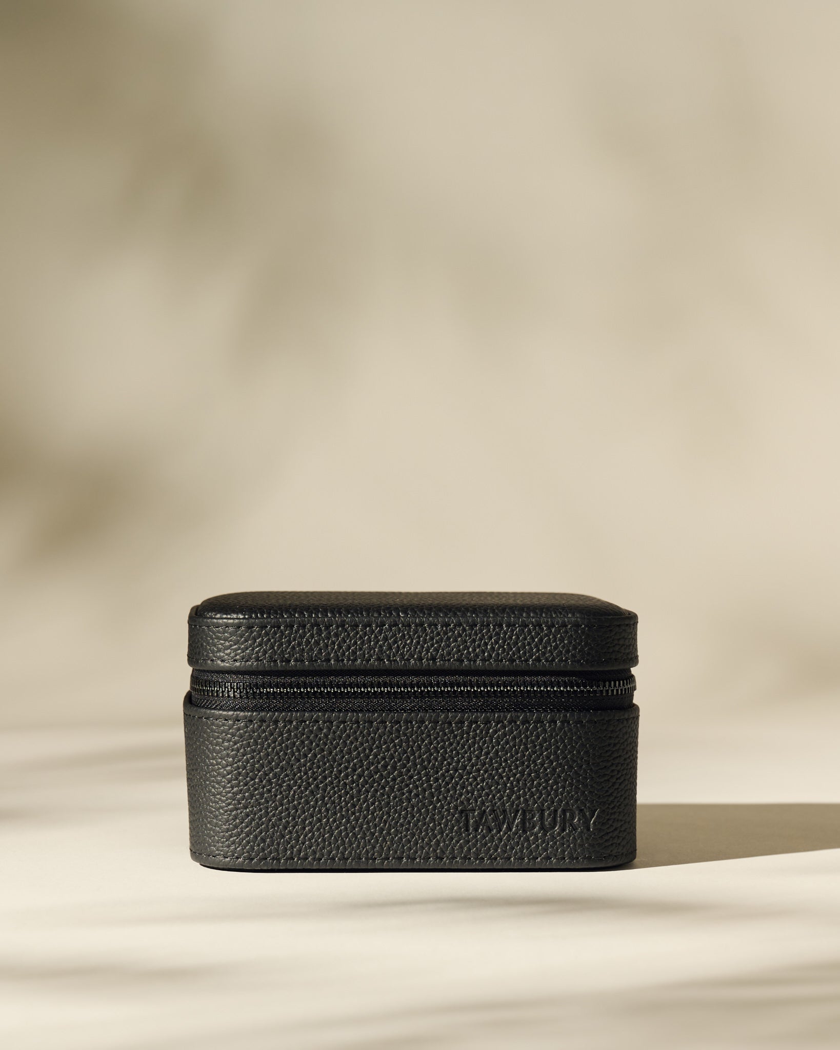 The TAWBURY Fraser 2 Watch Case in black leather with a textured finish rests on a neutral surface, highlighted by soft, diffused lighting and subtle shadows.