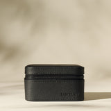 The TAWBURY Fraser 2 Watch Case in black leather with a textured finish rests on a neutral surface, highlighted by soft, diffused lighting and subtle shadows.