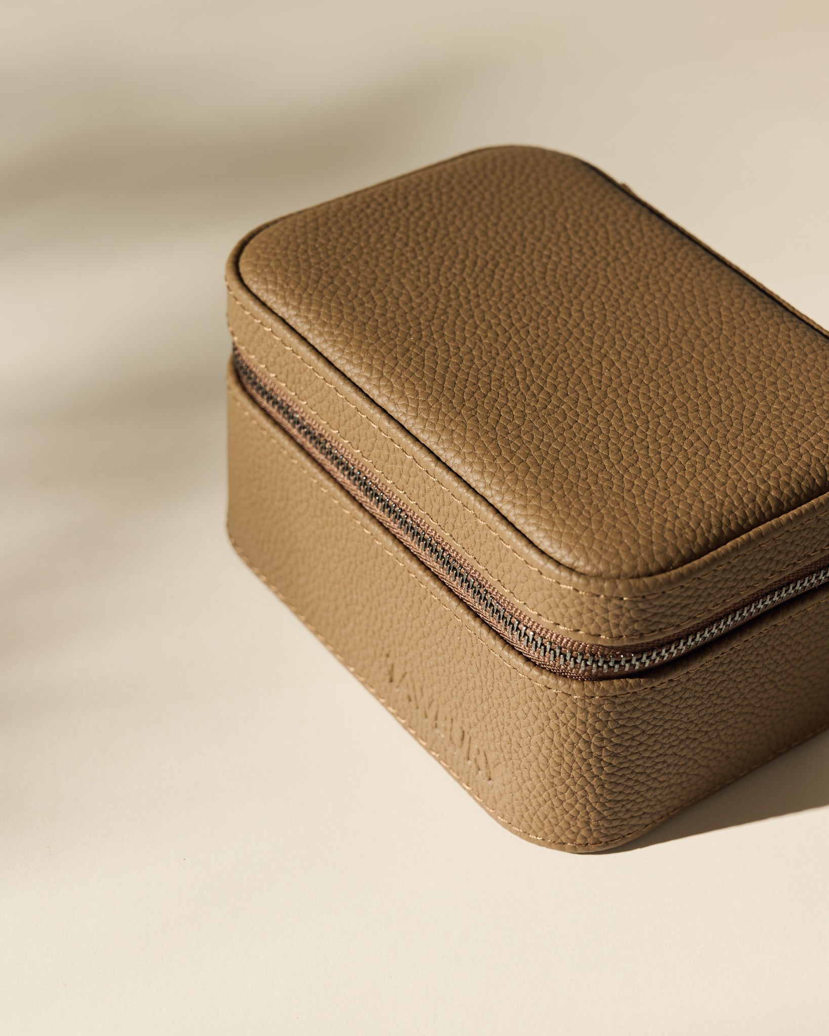 The TAWBURY Fraser 2 Watch Case in taupe, featuring a compact rectangular design and zippered closure, rests on a neutral surface under soft lighting.